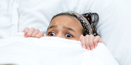 scared girl peeking out from under the covers